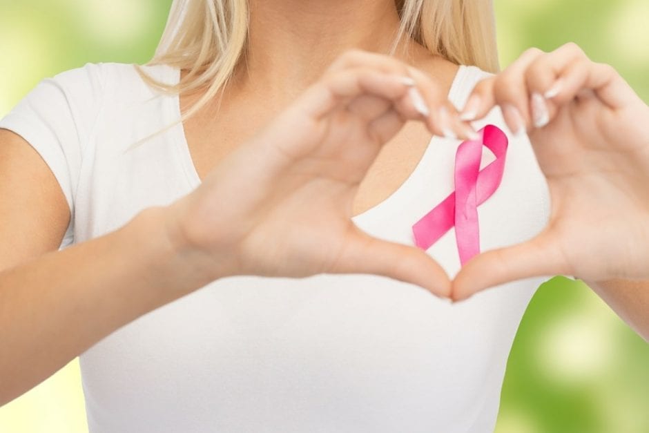 woman making the heart symbol with hands over the breast awareness ribon