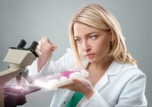 Young female microscopist in white coat selects a tissue sample